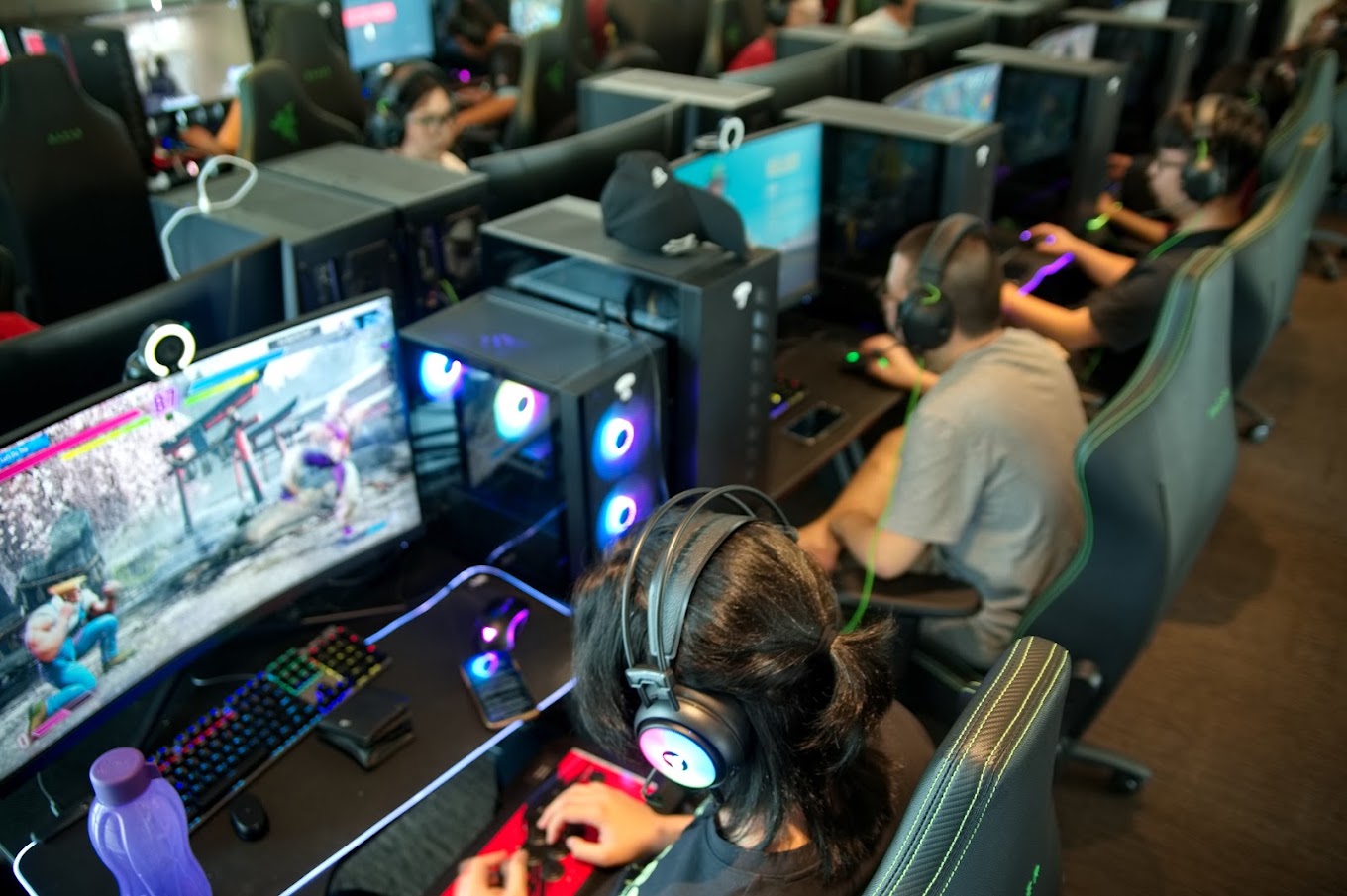 back view of woman wearing headphones gaming on pc computer in titan esports gaming